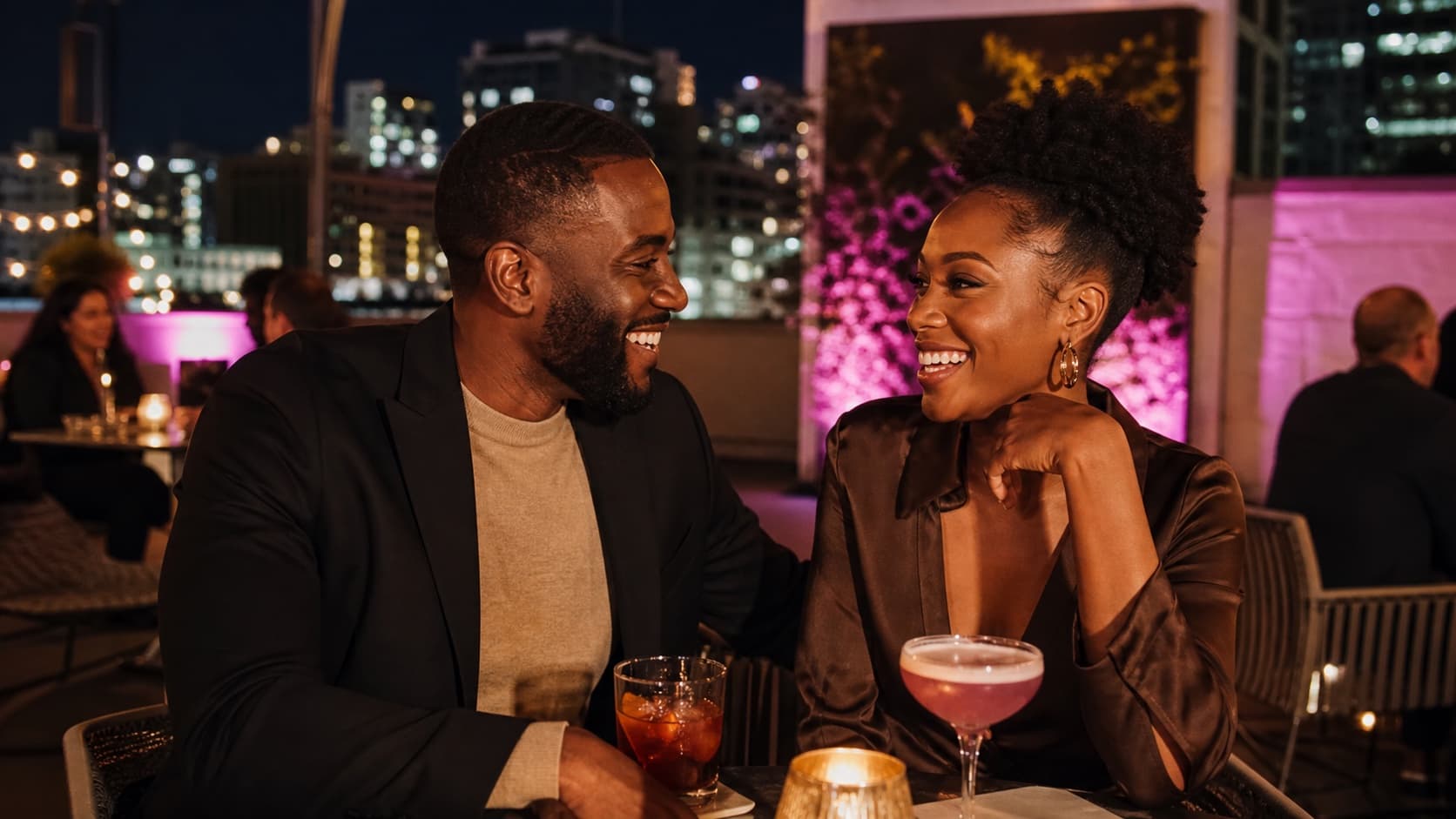 A Black couple laughing together over cocktails at a Kansas City rooftop bar